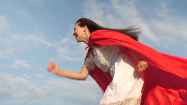 funny superhero girl run and laugh in red cloak, cloak fluttering in wind. Cheerful young woman plays in super hero. girl dreams of becoming a superhero. girl in a red cloak expression of dreams.