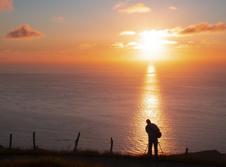 Fototapeta premium Man photographing the sun over the sea at sunset, Basque Country