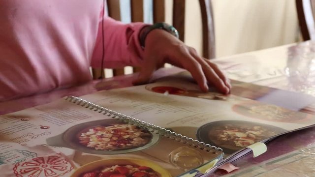 A young lady casually flipping through a colorful recipe/cook book.
