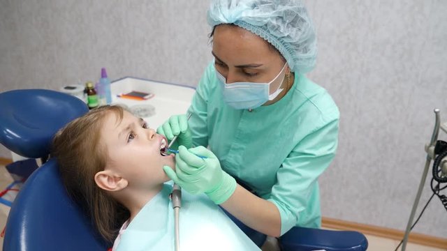 Doctor dentist of Asian appearance treats a little girl’s teeth with a special filling photopolymer substance. Healthcare concept in 4K video.
