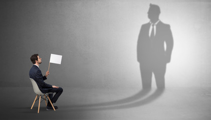 Humble businessman staying and offering stuffs to a huge businessman shadow
