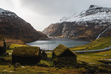 Typical Faroese grass-covered cabins in the small village Saksun during early spring with snow-covered mountain ranges and dark blue sea (Faroe Islands, Denmark, Europe