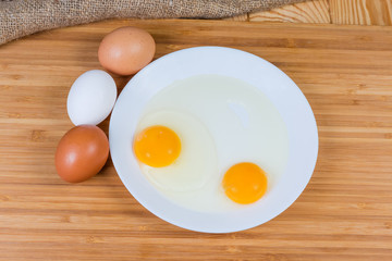 Two broken eggs on dish and whole eggs, top view