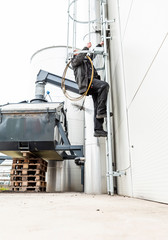 Chimney sweep cleaning a chimney standing balanced on the apex of a house roof lowering equipment down the flue