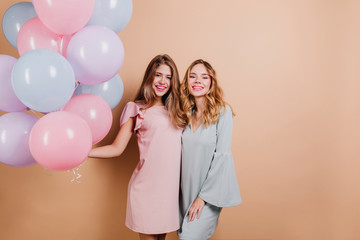 Fascinating birthday girl in pink outfit enjoying celebration. Studio shot of elegant ladies holding balloons and laughing on light background.