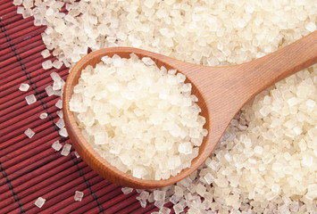 Wooden spoon and sugar on red bamboo mat background