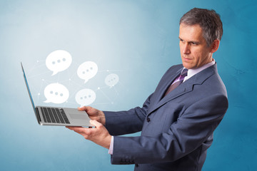 Man holding laptop with a few speech bubble symbols
