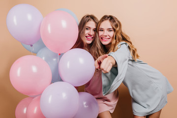 Fototapeta na wymiar Pretty girls with trendy makeup having fun at birthday party. Emotional caucasian ladies with balloons waiting for event.
