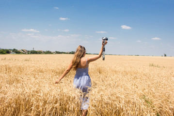 woman in a blue dress with a camera on a wheat field sky