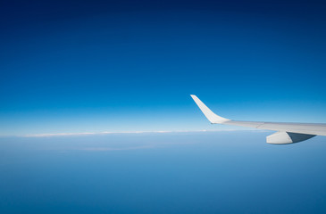 Wing of plane over white clouds. Airplane flying on blue sky. Scenic view from airplane window. Commercial airline flight. Plane wing above clouds. Flight mechanics concept. International flight.