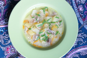 Meat soup with couscous with potato, carrot, tomato, spices, greenery in light green plate on colorful background