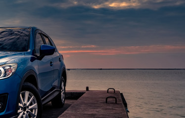 Fototapeta na wymiar Blue compact SUV car with sport and modern design parked on concrete road by the sea at sunset in the evening. Hybrid and electric car technology concept. Car parking space. Automotive industry.