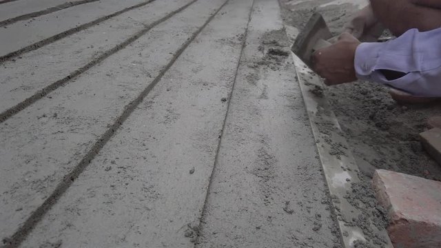 Indian mason working on a cement pathway with parallel lines on the side of the road street. 4k slow motion stabilized gimbal handheld close-up