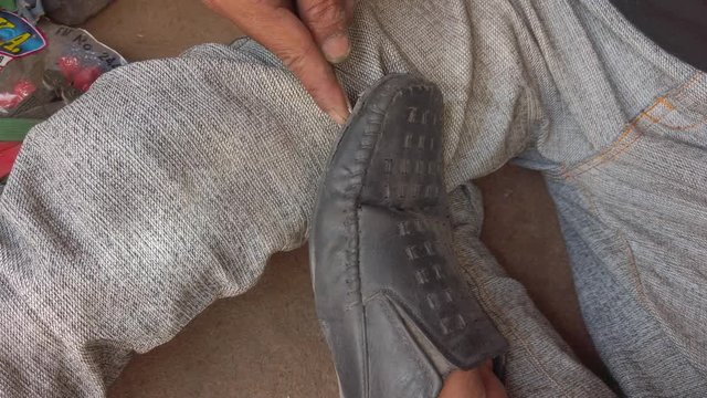 Indian street scene of a cobbler's hands mending footwear both leather shoe and fancy female sandal as he sits on the roadside stitching with needle and thread 4k stabilized gimbal close-up handheld