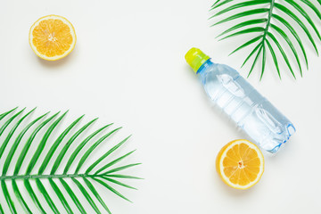 Tropic leaves and bottle l water on yellow background. Detox fruit infused water.