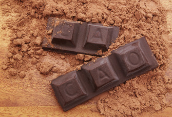 Chocolate bars with word CACAO and cacao powder on wooden background