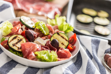 Fresh lettuce salad with grilled zucchini coppa di parma ham feta cheese olives tomatoes and olive oil