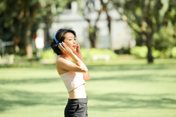 Beautiful attractive young Asian woman listening to her favourite song in headphones and singing when walking in park