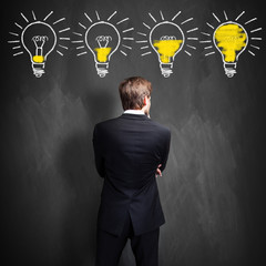 successful businessman standing in front of a blackboard with lightbulbs, symbolizing having an...