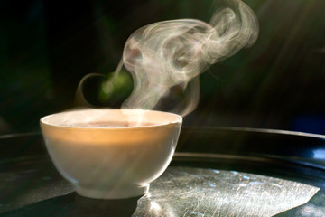 White bowl of hot soup with smoke and flare light served on metal tray for breakfast with copy space.
