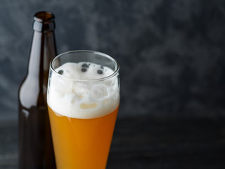 A glass of wheat unfiltered beer on a dark table and a beer bottle. copy space