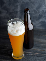 A glass of wheat unfiltered beer on a dark table and a beer bottle
