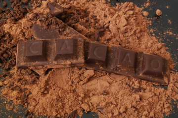 Chocolate bars with word CACAO and cacao powder on black table