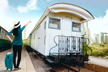 Rear view of asian woman in hat with suitcase bag standing and pointing a white train wagon on station