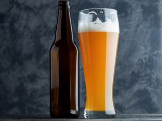 A glass of wheat unfiltered beer on a dark table and a beer bottle