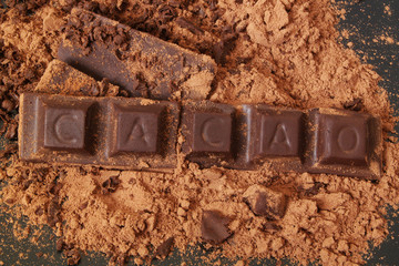 Chocolate pieces with word CACAO on and cacao powder background