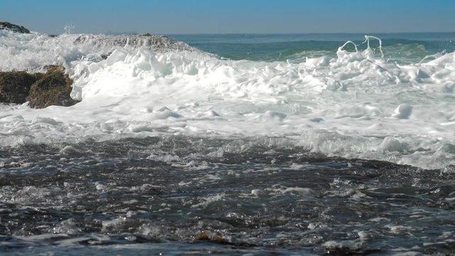 foaming ocean waves roll on brown rock near coastline on sunny summer day slow motion. Concept tsunami impact and ecosystem change