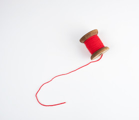 wooden bobbin with red wool threads on a white background
