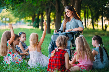 Fototapeta premium Disabled teacher conducts a lesson with children in nature. Interaction of a teacher in a wheelchair with students.