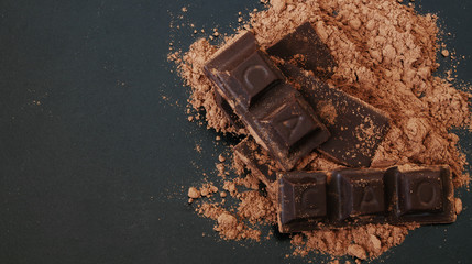 Chocolate bars with word CACAO and cacao powder on black table with space for text