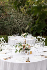 Wedding table setting decorated with fresh flowers in a brass vase. Wedding floristry. Banquet table for guests outdoors with a view of green nature. Bouquet with roses, eustoma and eucalyptus leaves