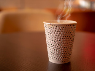 Paper cup with hot coffee or tea on a table in a cafe