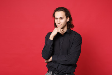 Handsome stylish young curly long haired man in black shirt posing isolated on red background studio portrait. People sincere emotions lifestyle concept. Mock up copy space. Put hand prop up on chin.