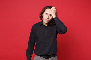 Young sad curly long haired man in black shirt standing posing isolated on red wall background studio portrait. People sincere emotions lifestyle concept. Mock up copy space. Problem crisis depression