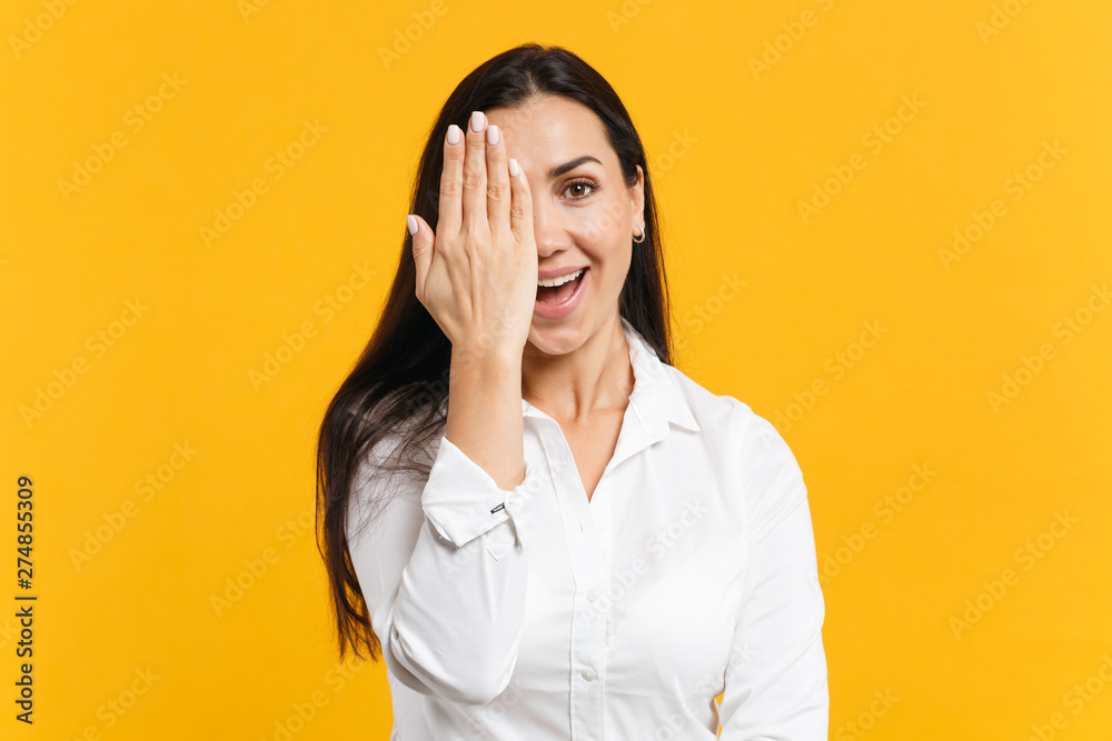 Wall mural portrait of cheerful joyful young woman in white casual shirt looking camera, covering face with han