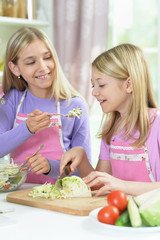 Two girls in pink aprons preparing salad