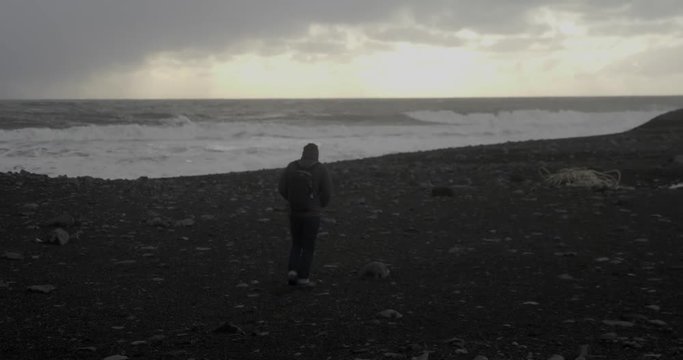 A traveler approaches the water of a black sand beach in Iceland.