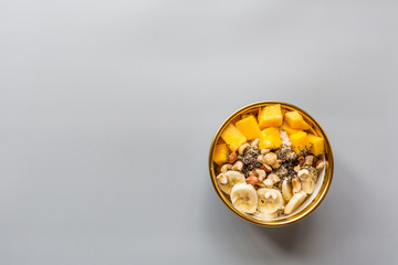 Breakfast oatmeal porridge with fresh fruits, chia seeds and hazelnut on gray background. Oatmeal with mango and banana. Healthy breakfast concept. Top view, flat lay, mockup, overhead, copy space