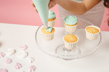 Close up cropped housewife female chef cook confectioner or baker in apron white t-shirt decorating cake cupcake at table isolated on pink pastel background in studio. Mock up copy space food concept.