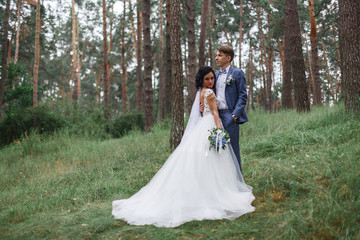 Groom in a suit holds bride in a white wedding dress outdoor.Happy young  newlyweds smiling on their wedding day.bride and groom hugging at the wedding in nature.wedding concept