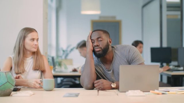 Tired Guy Falling Asleep With Laptop. Colleague Giving Coffee To Sleepy Man.