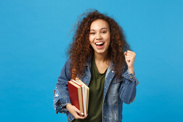 Young african american girl teen student in denim clothes, backpack hold books isolated on blue...