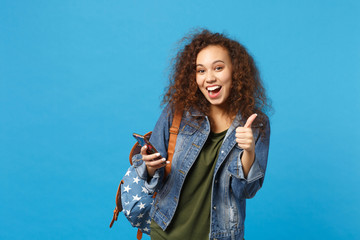 Young african american girl teen student in denim clothes, backpack hold phone isolated on blue wall background studio portrait. Education in high school university college concept. Mock up copy space