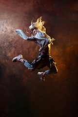 Fototapeta na wymiar Photo of jumping blonde dancer woman looking back in torn jeans and sneakers on dark brown background