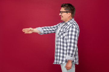 Fototapeta premium side view portrait of happy excited middle aged business man in casual checkered shirt, eyeglasses standing, giving hand to handshake and greeting. indoor studio shot, isolated on dark red background.