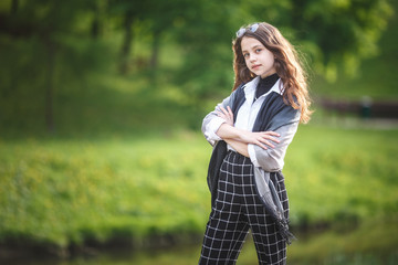 portrait of little beautiful stylish kid girl with sunglasses and short plaid pants in city park on green forest background